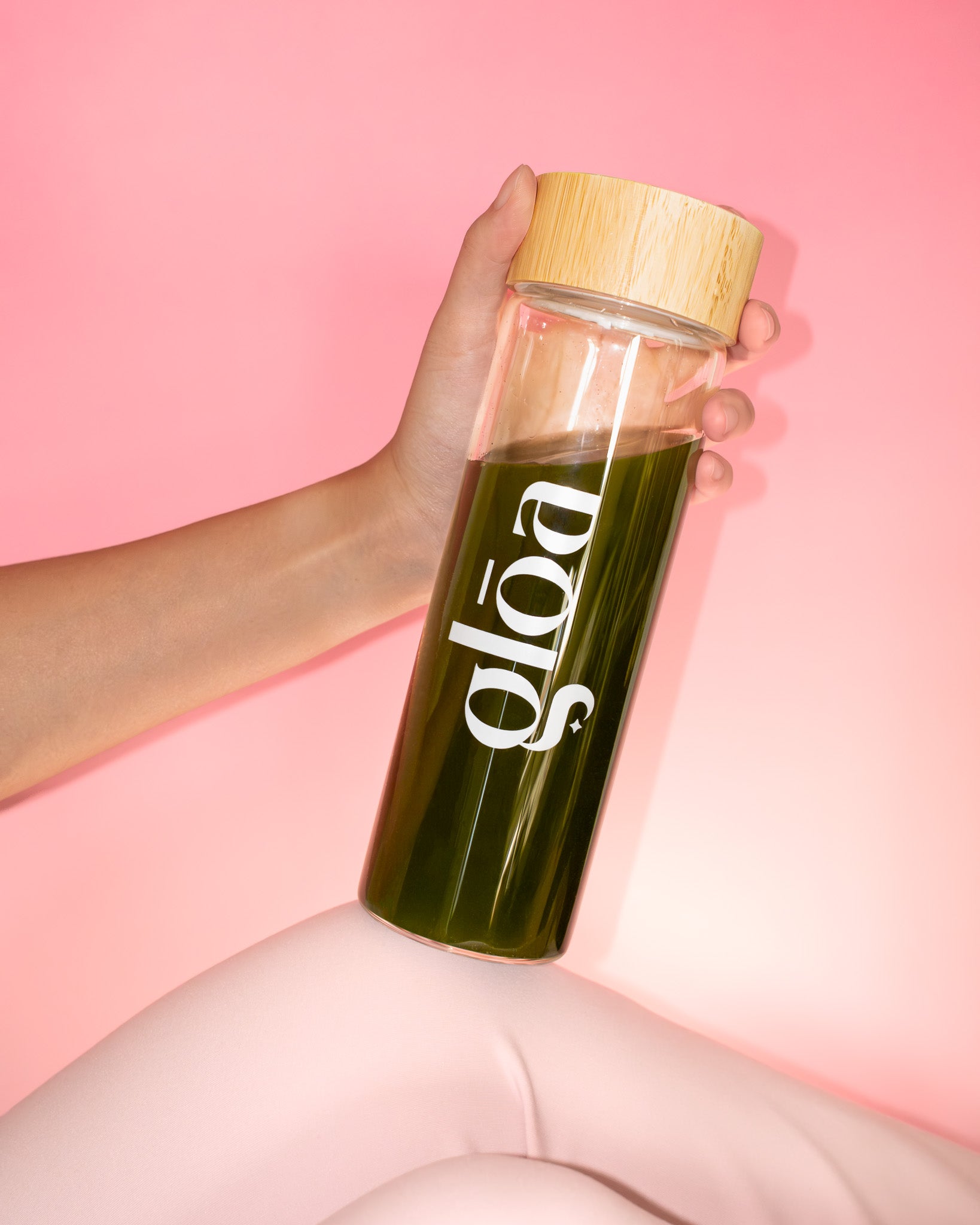 Skleněná lahev Gloā s bambusovým víčkem naplněná zeleným nápojem Supergreens v ženské ruce. Stylový a zdravý lifestyle doplněk pro každodenní energii a krásu.